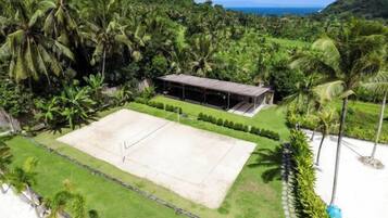 A tennis court surrounded by lush greenery and a small building with a roof.