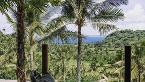 Una habitación con vistas a un paisaje exuberante, con palmeras y una vista distante del océano.