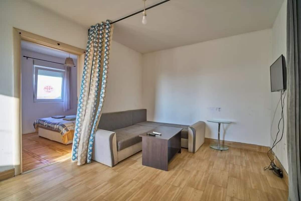 A modern room with a sofa, a small table, a TV, and a window with curtains.