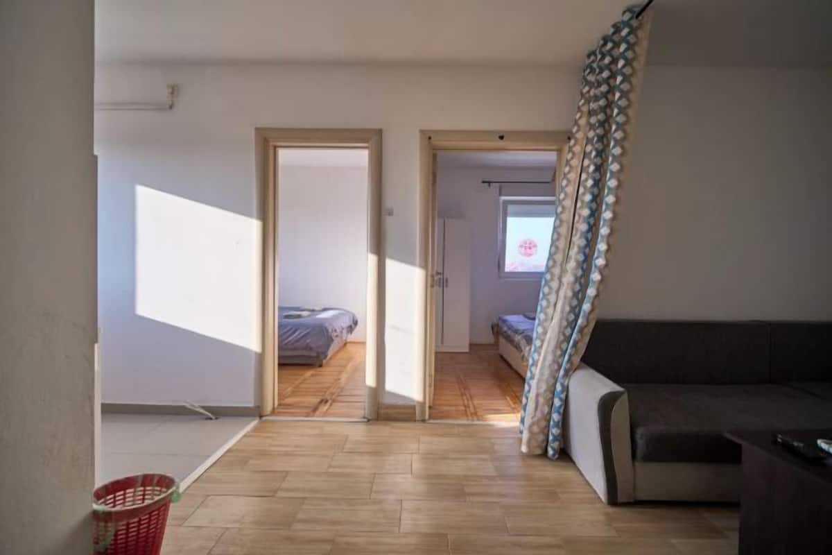 An open-plan living space with a sofa, a bed, and a window with curtains.