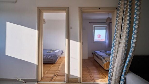 Ein Zimmer mit Holzboden, zwei Betten, einem Fenster mit Ausblick und einer Tür zu einem anderen Raum.