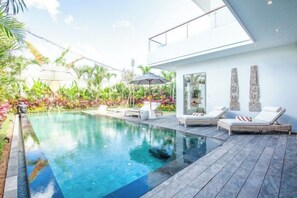 A modern outdoor pool area with lounge chairs and a glass-enclosed room. - Villa ARNAUD 17 (Bali)