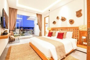 A modern hotel room with a large bed, a TV, a desk, and a balcony with a city view. - Villa ARNAUD 17 (Bali)