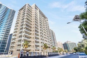 A multi-story building with balconies, a street in front, and other buildings in the background. - bnbme Great Value Apt in Dubai Sports City (Dubai)