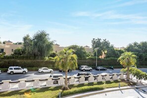A parking lot with multiple cars, a palm tree, and a building in the background. - bnbme Great Value Apt in Dubai Sports City (Dubai)