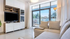 A modern living room with a large window, a flat-screen TV, and a sofa. - bnbme Great Value Apt in Dubai Sports City (Dubai)
