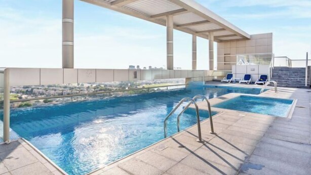A rooftop pool with clear blue water, a covered seating area, and a view of the cityscape. - bnbme Great Value Apt in Dubai Sports City (Dubai)