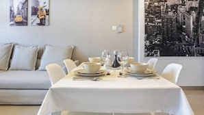 A dining area with a white table set for four, white chairs, and a sofa in the background. - bnbme Great Value Apt in Dubai Sports City (Dubai)