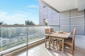 A balcony with a wooden table and chairs, a glass railing, and a view of a residential area. - bnbme Great Value Apt in Dubai Sports City (Dubai)