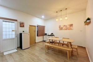 A compact kitchen with a refrigerator, a dining table with benches, and hanging pendant lights. - Sleeping Shine by DeliZia Homestay (9-10 Persons) (Satun)