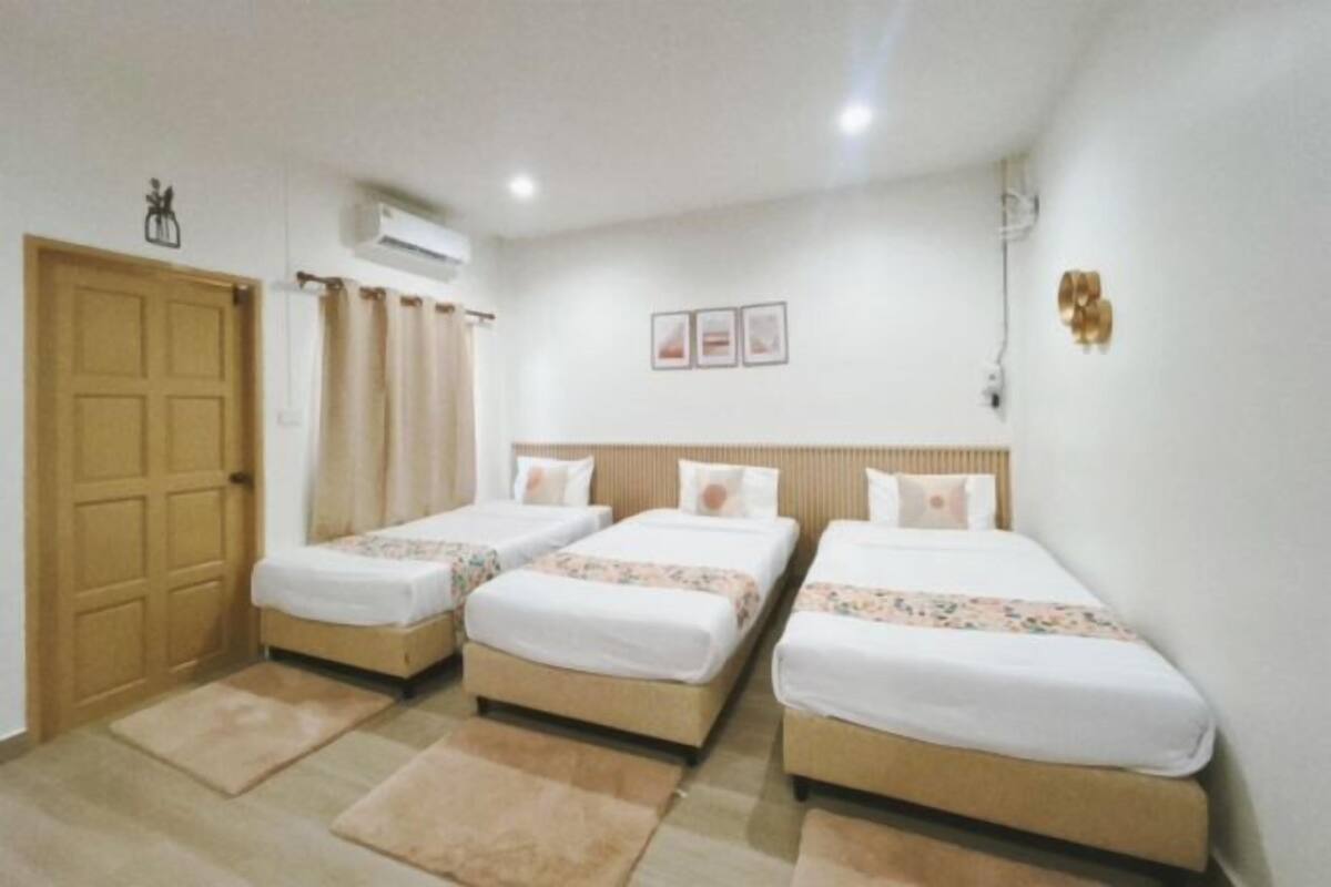A hotel room with three single beds, a wooden door, an air conditioning unit, and a wall-mounted light fixture.