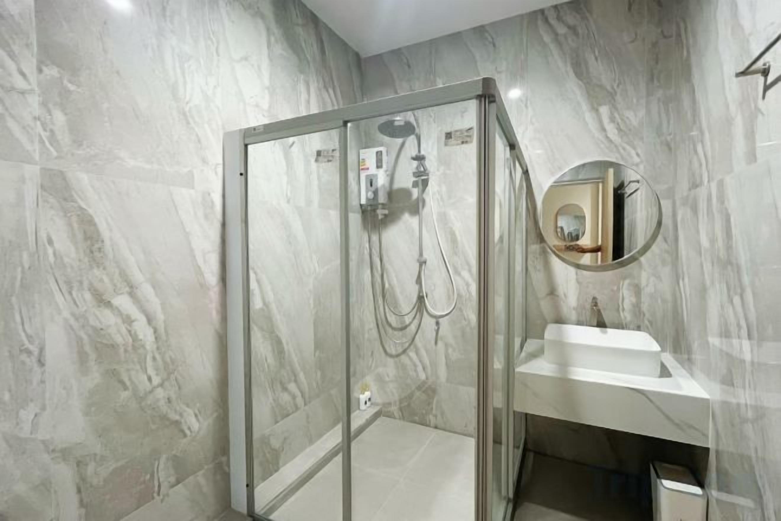 Ein Badezimmer mit einer Duschkabine aus Glas, einem weißen Waschbecken und einer Marmorwand.
