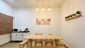 A dining area with a wooden table and benches, a kitchen area with cabinets and appliances, and a wall-mounted shelf with plants.
