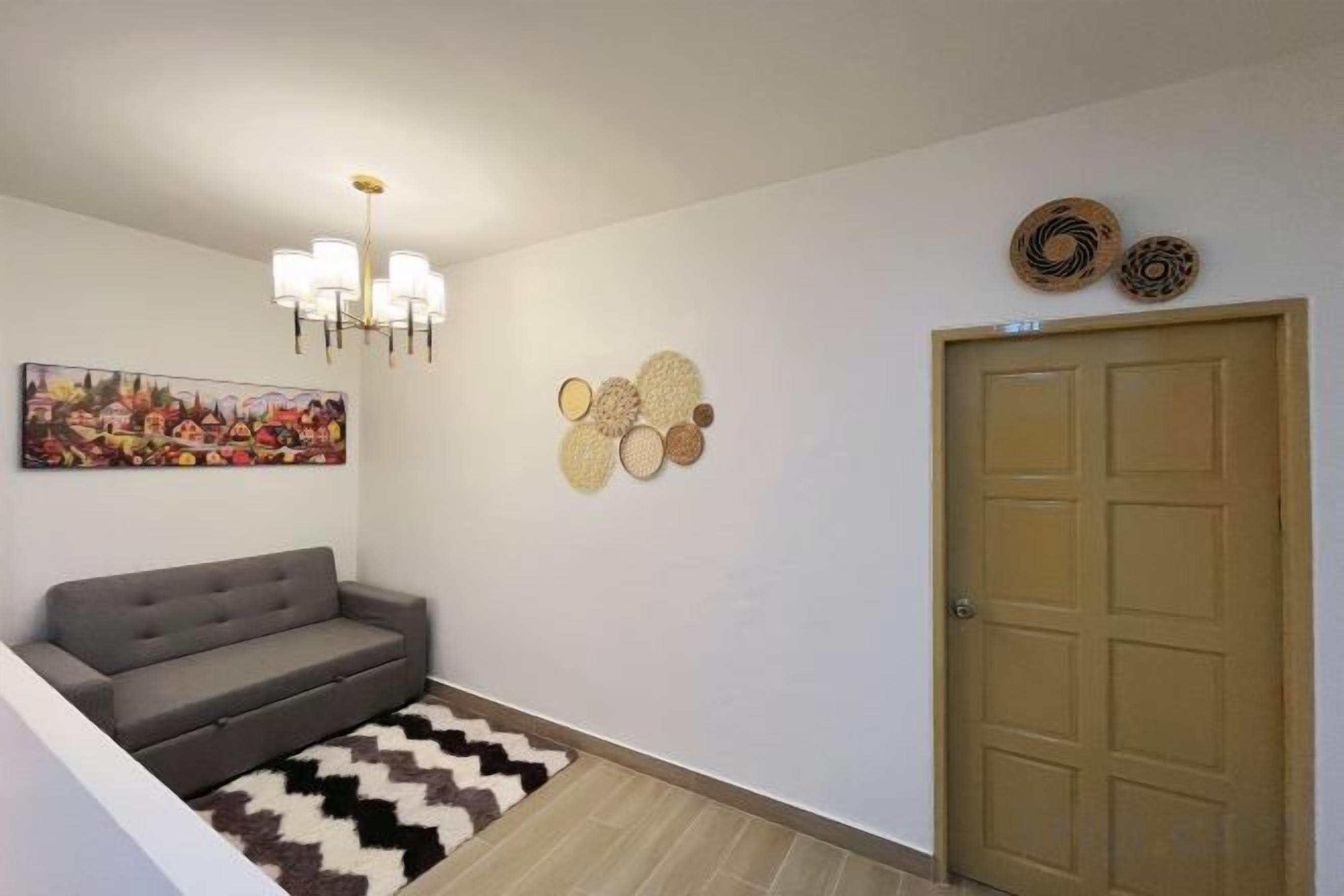 Ein Flur mit einem grauen Sofa, einem gemusterten Teppich, einer Chandelüster, Wandbildern und einer Tür.
