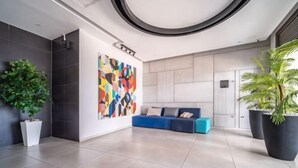 A modern lobby with a blue sofa, a colorful abstract wall art, and large potted plants. - Achziv Beach Haven 3BR Apartment by Sea N' Rent (Nahariyya)