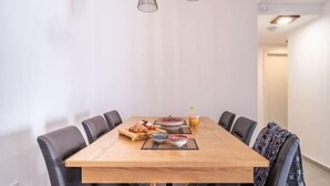 A dining area with a wooden table, black chairs, and a small breakfast spread including bread, fruit, and a bowl of cereal. - Achziv Beach Haven 3BR Apartment by Sea N' Rent (Nahariyya)