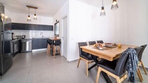 A modern kitchen with a dining area, featuring a wooden table and chairs, a refrigerator, and a sink. - Achziv Beach Haven 3BR Apartment by Sea N' Rent (Nahariyya)