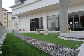 Un bâtiment moderne doté d’un chemin pavé, d’un espace extérieur aménagé pour s’asseoir et offrant une vue dégagée sur l’intérieur grâce à de grandes fenêtres.