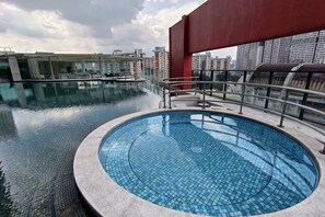 Une piscine sur le toit, dotée d’une paroi en verre et offrant une vue sur le paysage urbain.
