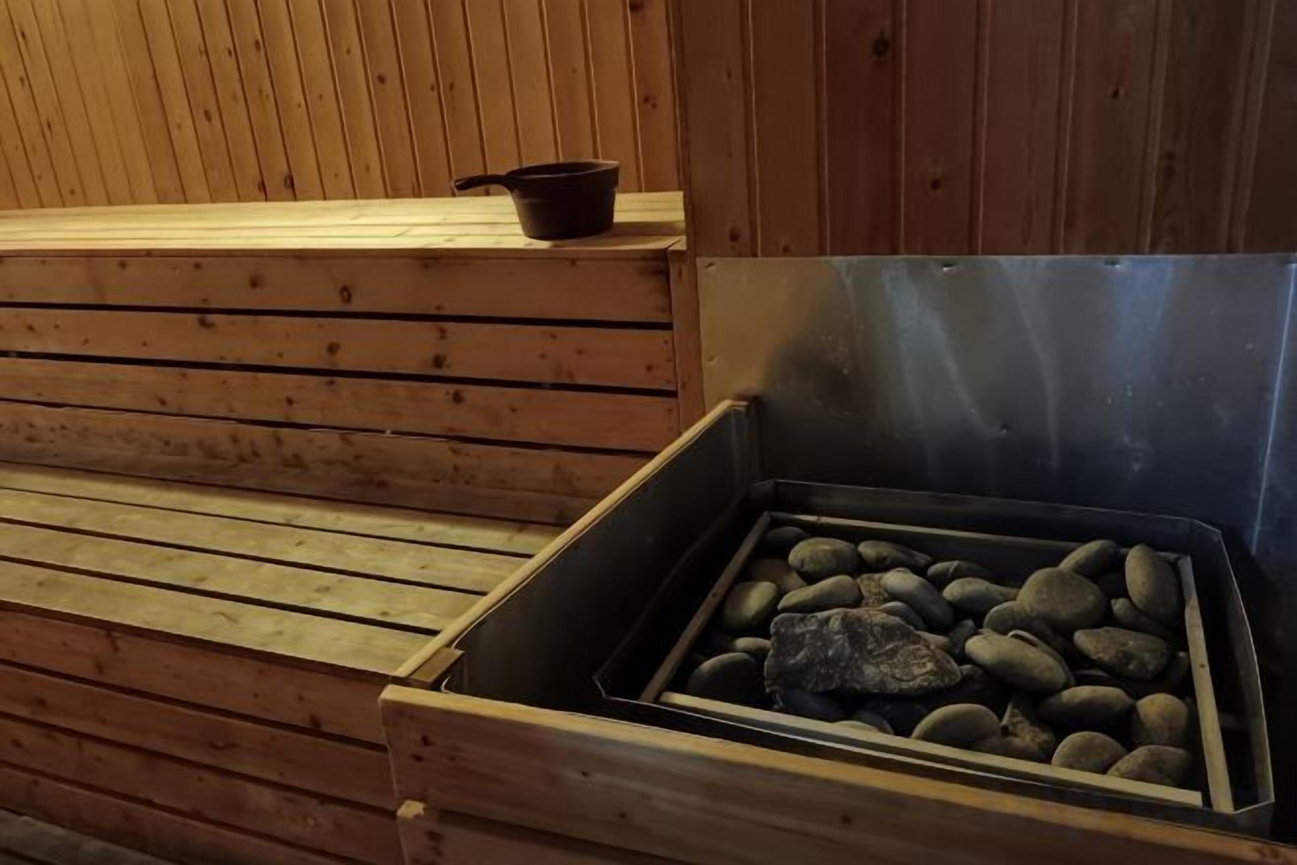 Una sauna con un banco de madera y un recipiente metálico lleno de piedras.
