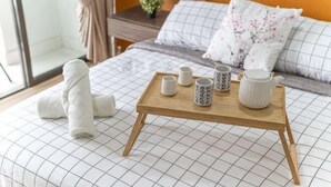 Un lit bien fait, recouvert d’une couverture à carreaux, un plateau en bois avec des tasses et une théière, et une paire de serviettes enroulées.