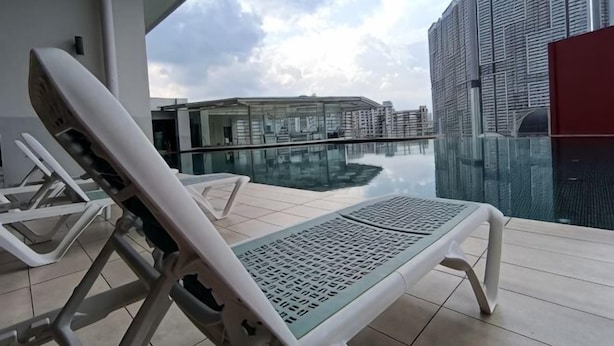 Un salon sur le toit, doté d’une piscine à débordement en verre, de chaises longues blanches et offrant une vue sur les gratte-ciel.