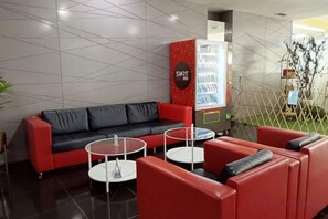 Un espace détente moderne avec un canapé rouge, deux tables basses blanches et un distributeur automatique.