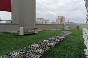 Une terrasse sur le toit, avec un revêtement de gazon synthétique, un chemin de galets et un banc.
