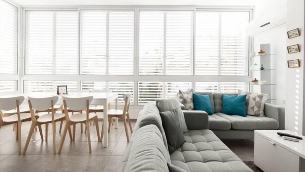 A modern living room with a grey sofa, white chairs, a dining table, and large windows with blinds. - Heart of Tel-Aviv Spacious Stay by Sea N' Rent (Tel Aviv)
