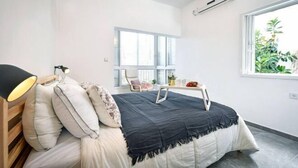 A bedroom with a bed, bedside lamp, window, and air conditioning unit. - Heart of Tel-Aviv Spacious Stay by Sea N' Rent (Tel Aviv)