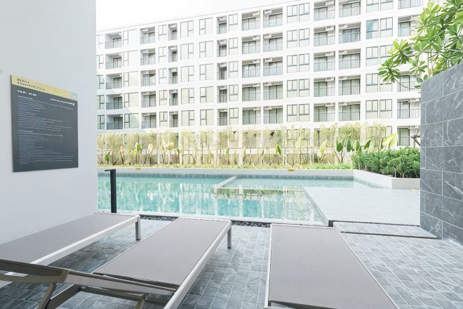 A swimming pool with lounge chairs, a high-rise building in the background, and a sign on the wall.