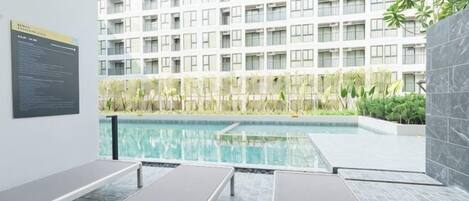 A swimming pool with lounge chairs, a high-rise building in the background, and a sign on the wall.