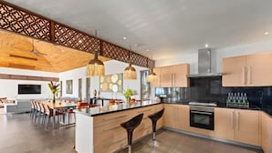 Een moderne keuken met een centraal eiland, hangende lampen en een eetgedeelte met stoelen.