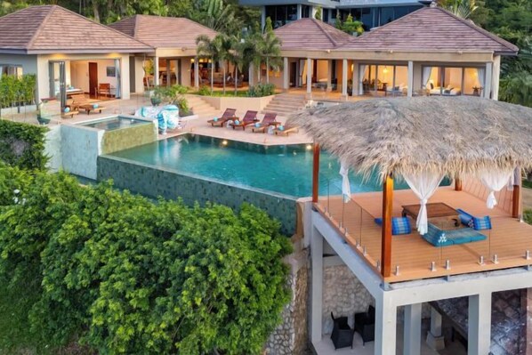 A resort with a swimming pool, lounge chairs, and a thatched-roof structure. - Baan Faasai 5-Bedroom Hillside Seaview Pool Villa (Koh Samui)