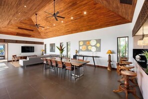 Amplia sala de estar con techo de madera, una mesa de comedor con sillas, un sofá y un televisor montado en la pared.