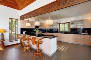 A modern kitchen with a central island, bar stools, pendant lighting, and a decorative ceiling panel. - Baan Faasai 5-Bedroom Hillside Seaview Pool Villa (Koh Samui)