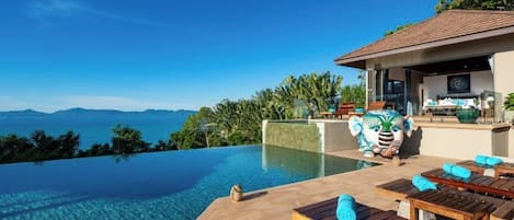 An infinity pool with a clear view of the mountains, wooden lounge chairs, and a covered seating area.