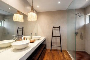 Un baño moderno con cabina de ducha de vidrio, suelo de madera y tocador blanco con dos lavamanos.