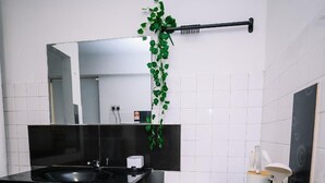 Een moderne badkamer met een zwarte wastafel, witte tegels, een spiegel en een groene plant.