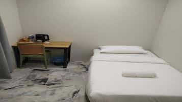 Una habitación pequeña con cama individual, escritorio, silla, un bote de basura y piso de baldosas.