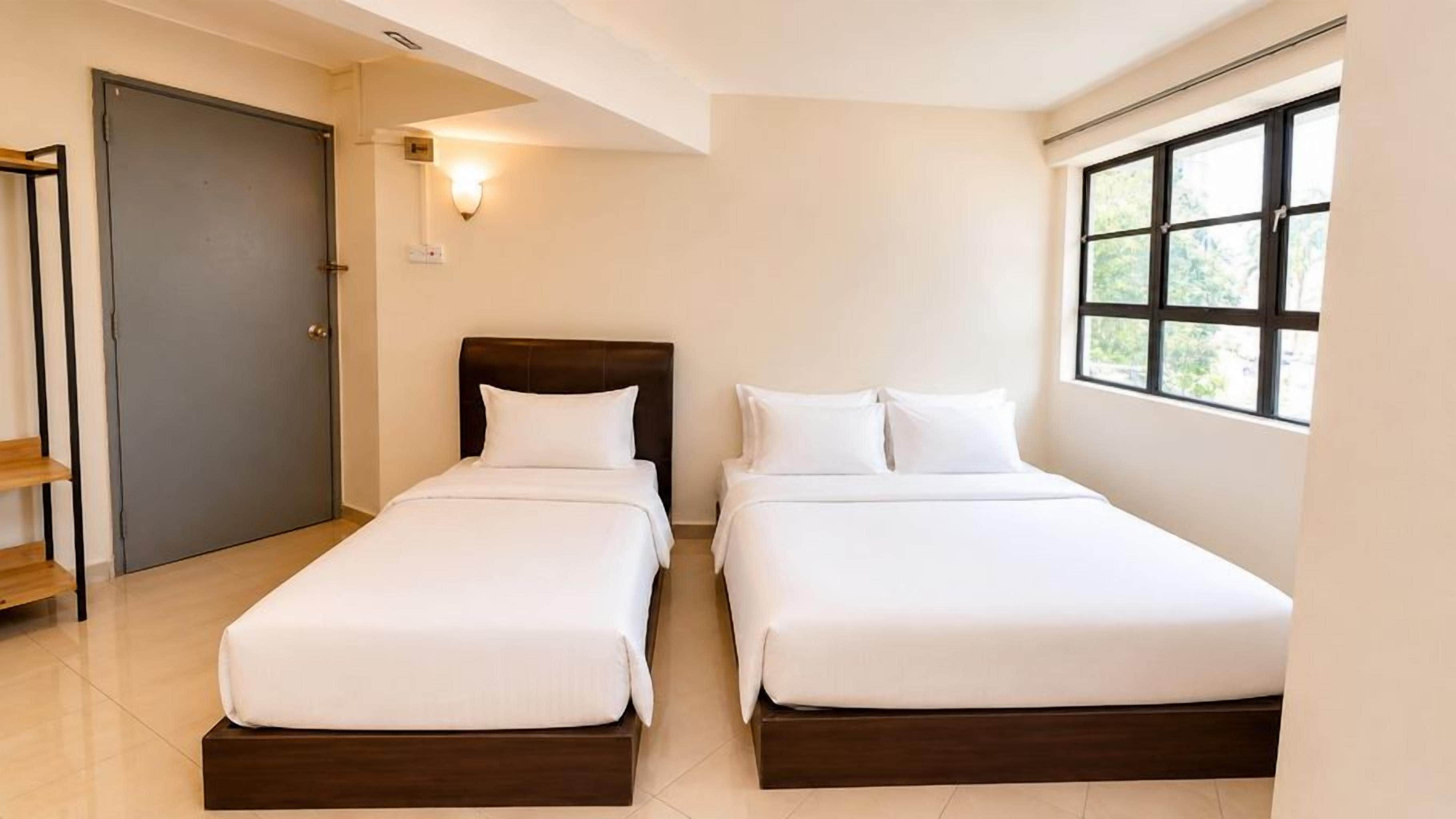 Una habitación de hotel con dos camas individuales, una puerta, un ventanal y una lámpara fijada a la pared.