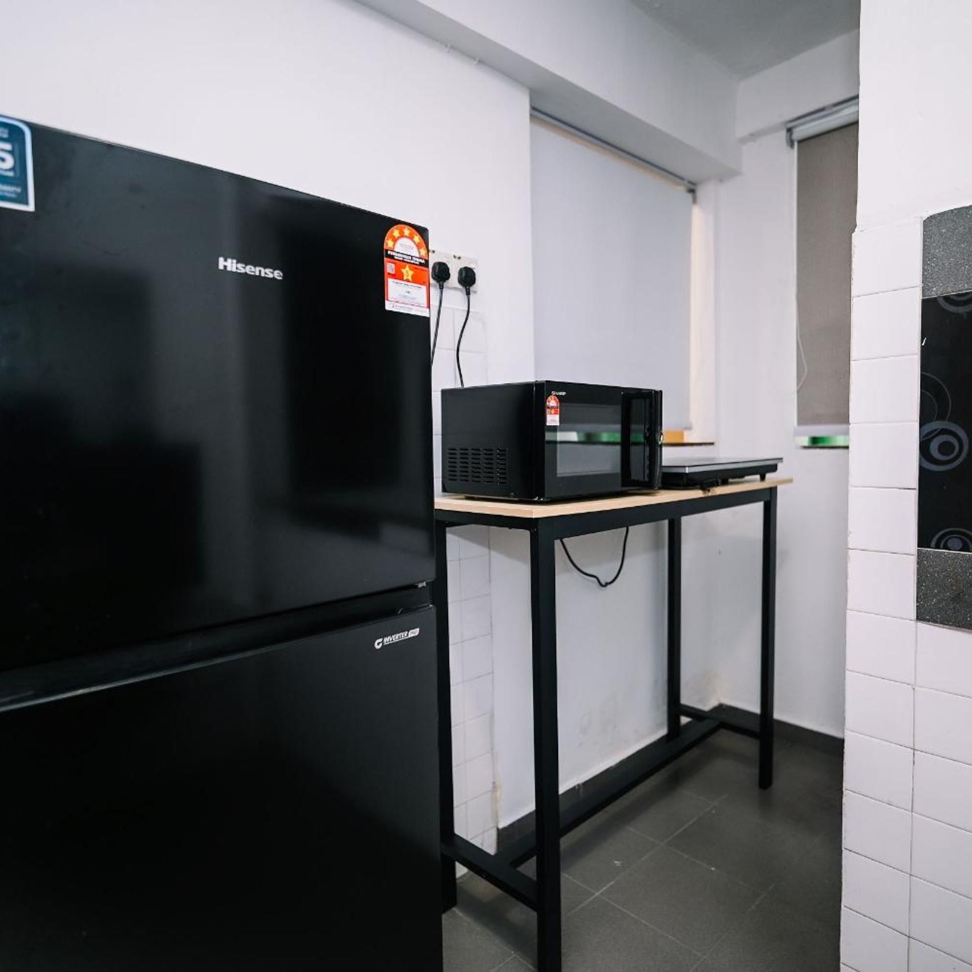 A kitchen with a black refrigerator, a microwave on a wooden table, and a white tiled wall.