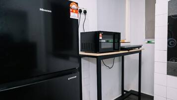 A kitchen with a black refrigerator, a microwave on a wooden table, and a white tiled wall.