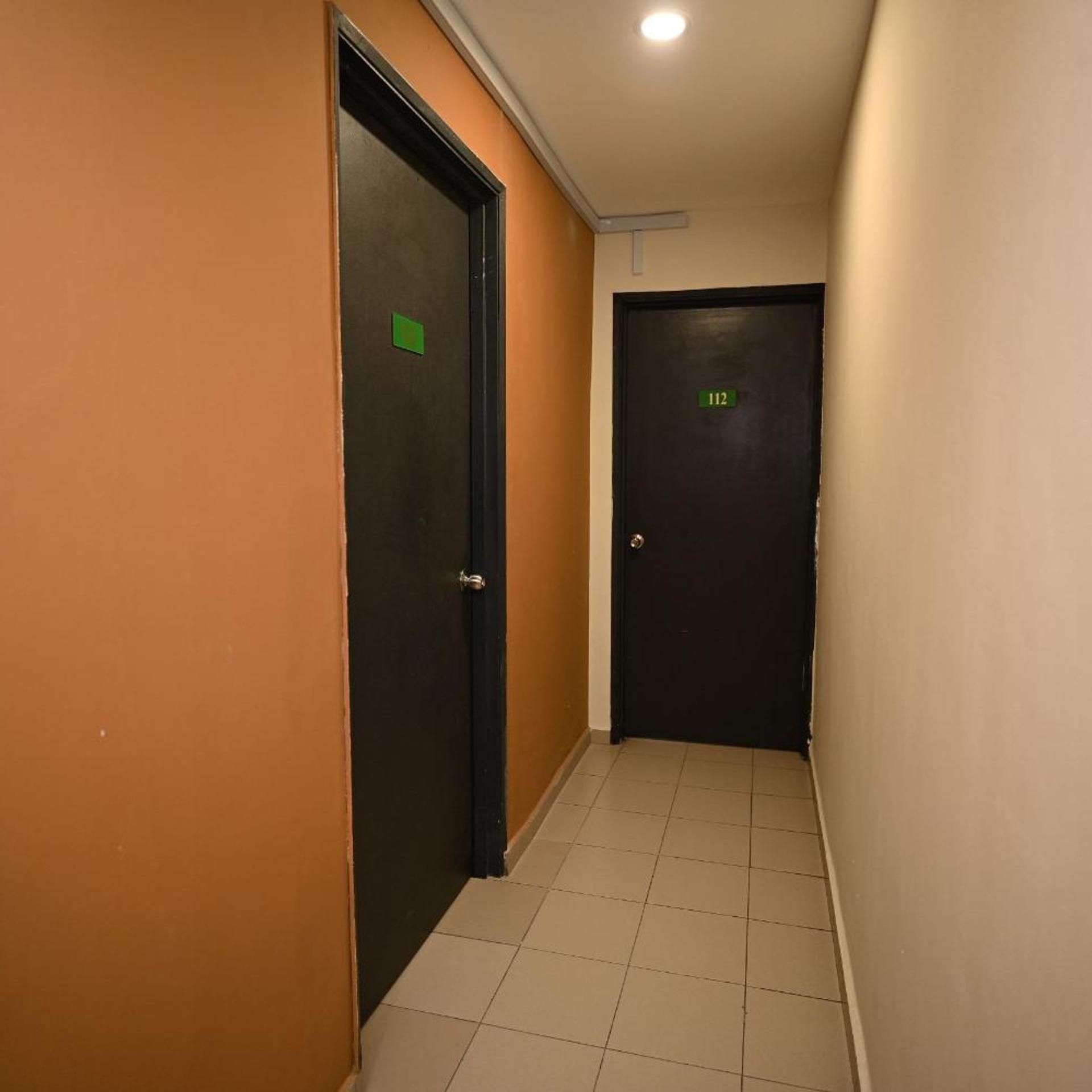 A corridor with two doors, one marked with the number 112, and a tiled floor.