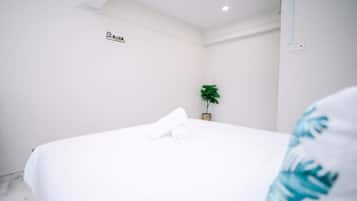 A hotel room with a neatly made bed, a small potted plant, and a sign on the wall.