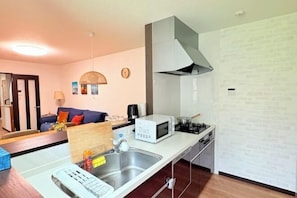 A compact kitchen with a microwave, stove, and sink. There is a dining area with a table and chairs, and a sofa in the background.