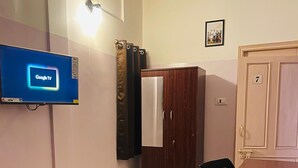 Une pièce équipée d’un téléviseur diffusant Google TV, d’un meuble en bois, d’une chaise rouge, d’une table et d’une porte portant le numéro 7.