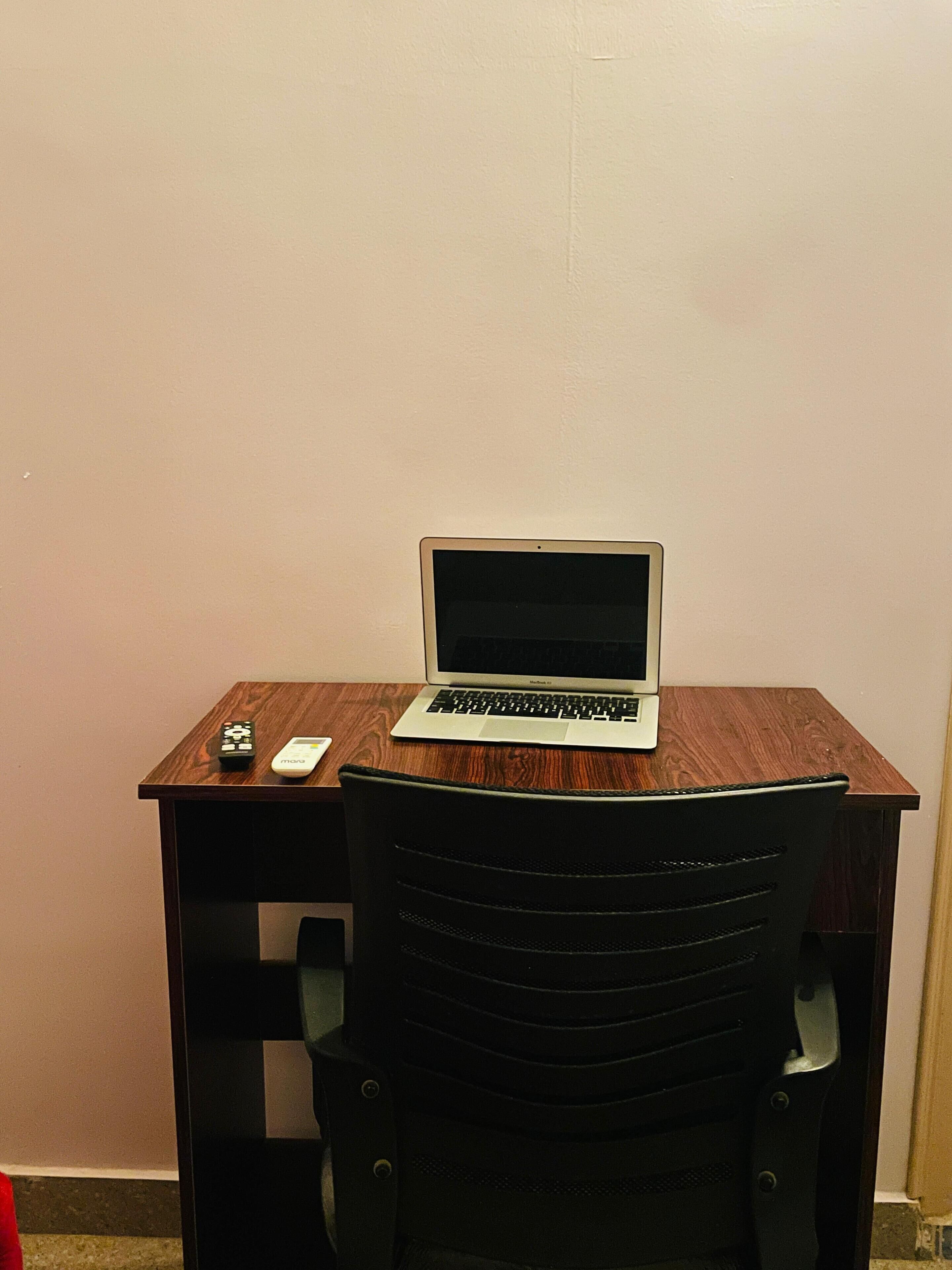 A laptop on a wooden desk with a chair in front.