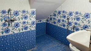 Une salle de bain avec des carreaux bleus à motifs floraux, un lavabo blanc et une douche dotée d’un robinet chromé.