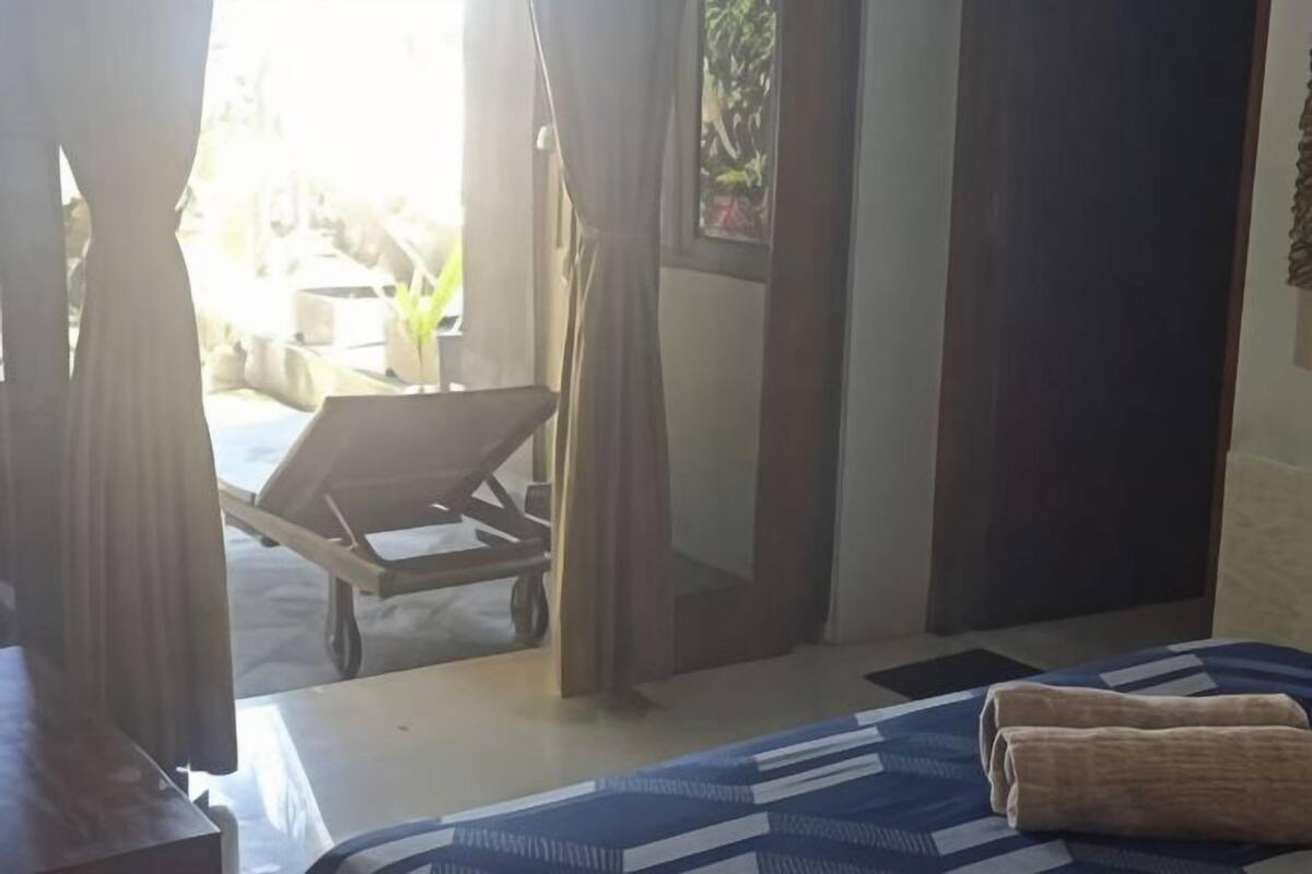 Un dormitorio con una cama, una silla de madera y vistas a un espacio exterior con una carretilla.